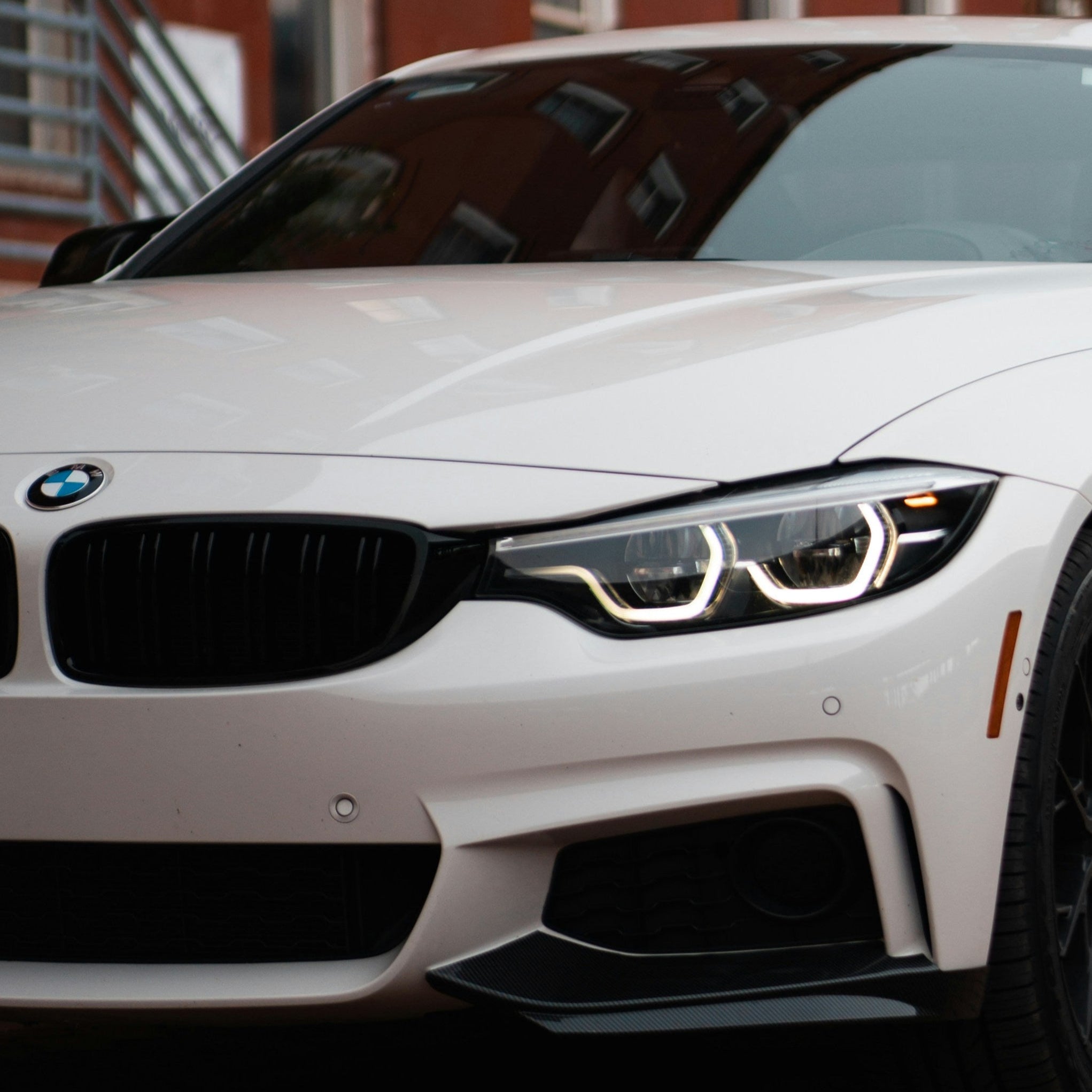 White BMW car parked on a brick street with red brick buildings in the background