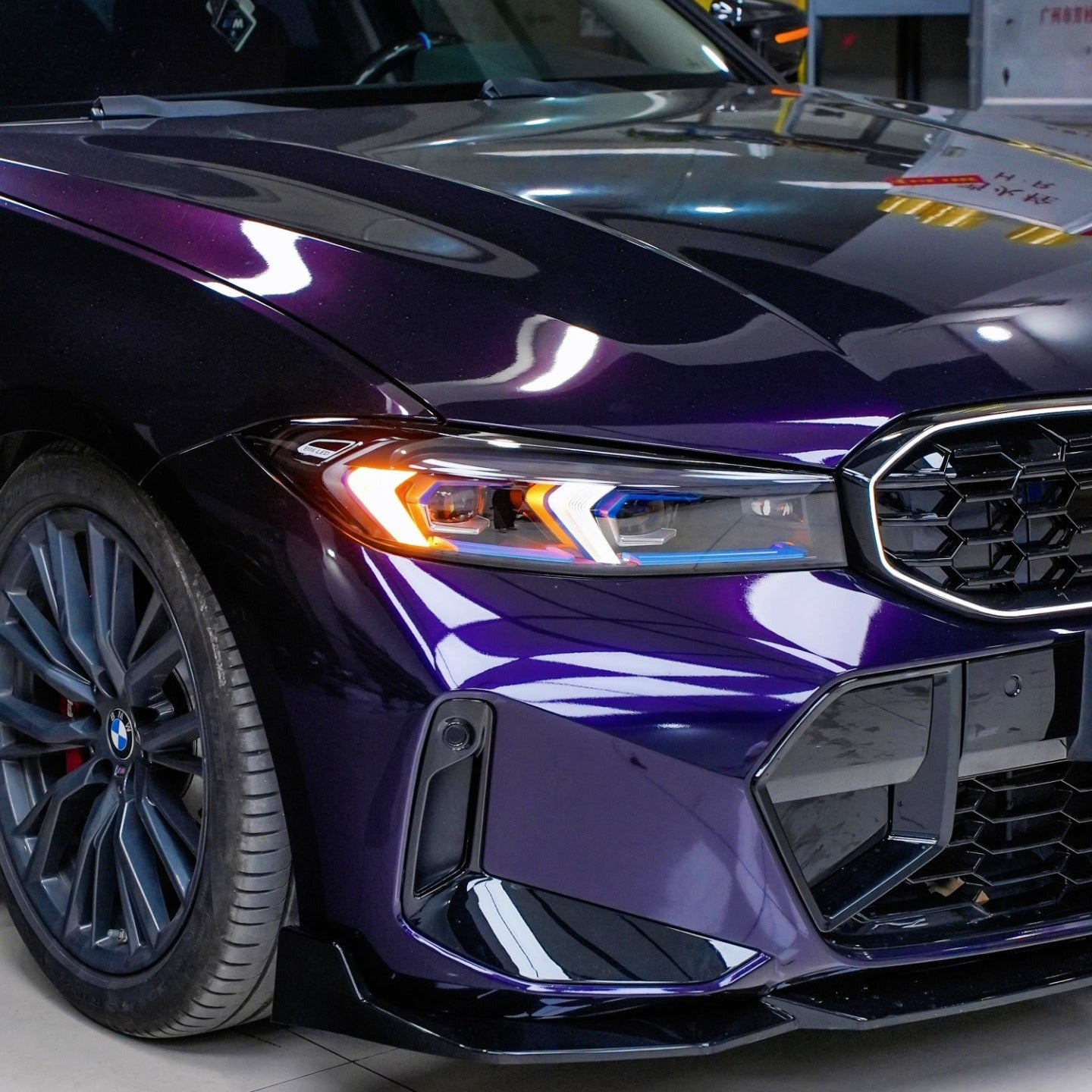 Close-up of a purple car's front grille and headlight in a garage setting