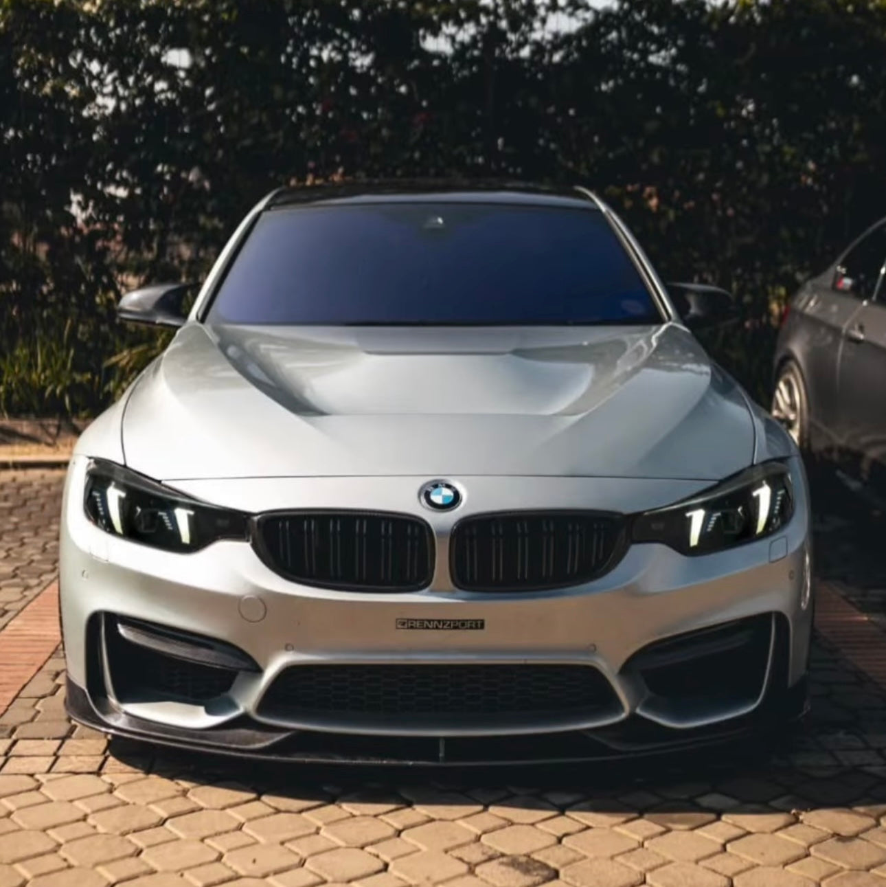 Front view of a silver BMW car on a brick driveway with trees in the background