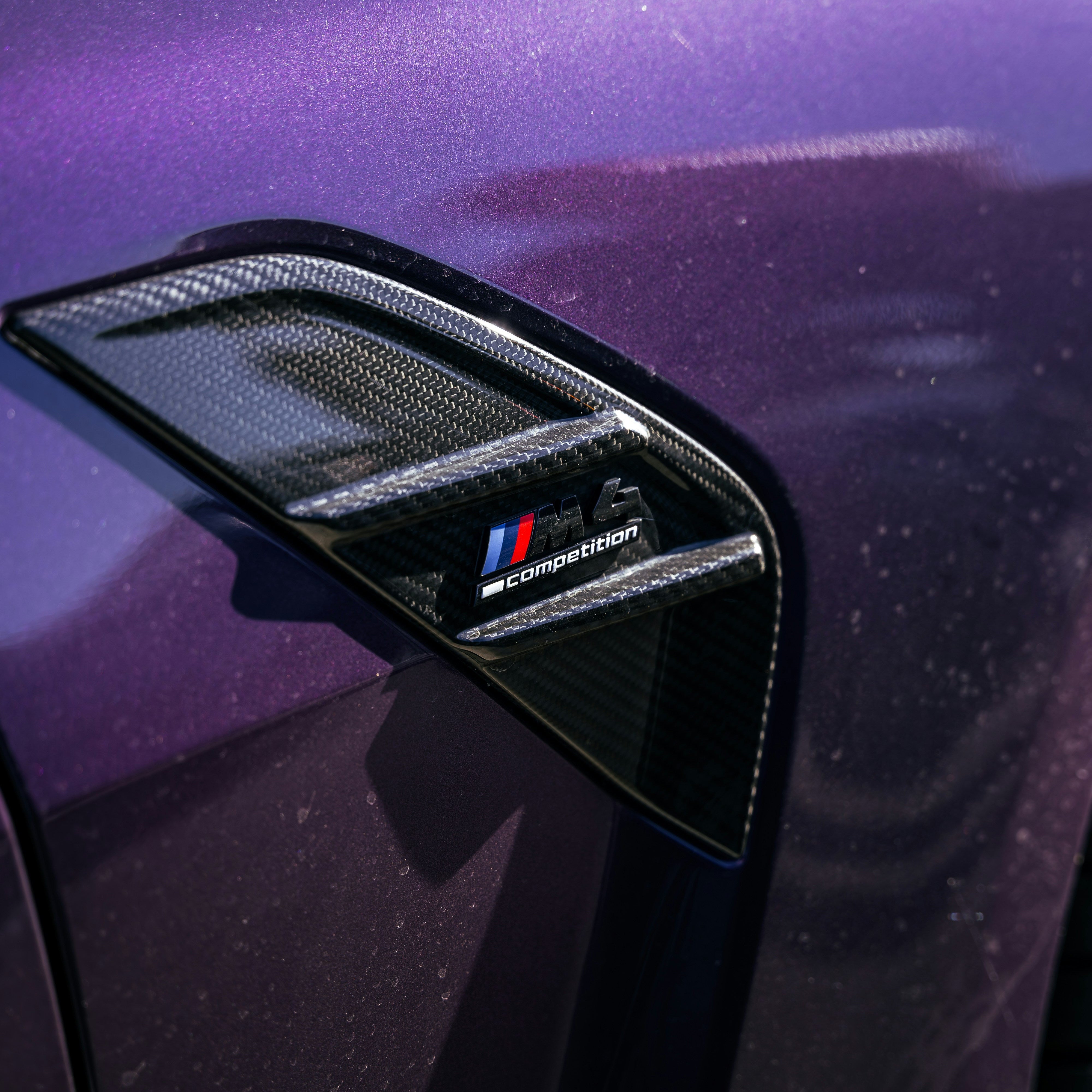Carbon fiber car spoiler with a logo on a purple car